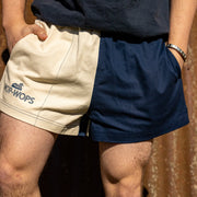 A person wearing a two-tone rugby shorts with one side in navy color and the other in cream, with the Wop-Wops logo on the front.